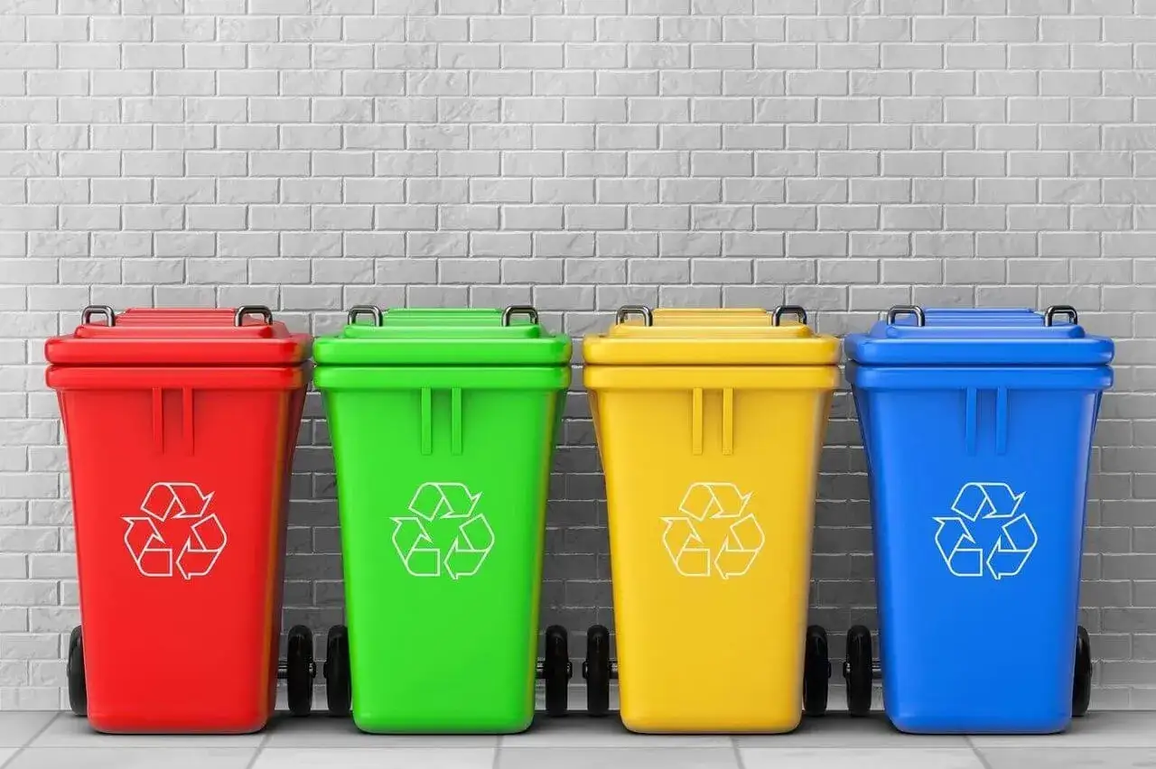 Cztery kolorowe kosze na śmieci (czerwony, zielony, żółty, niebieski) z symbolami recyklingu. Uczą, jak segregować śmieci.